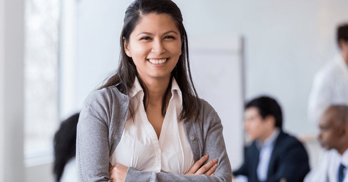 Happy employee with brown hair, arms crossed, grey sweater