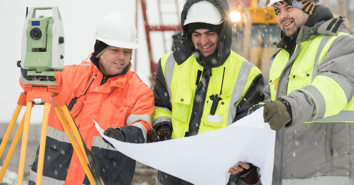 Construction employees in hardhats, looking over a large piece of paper