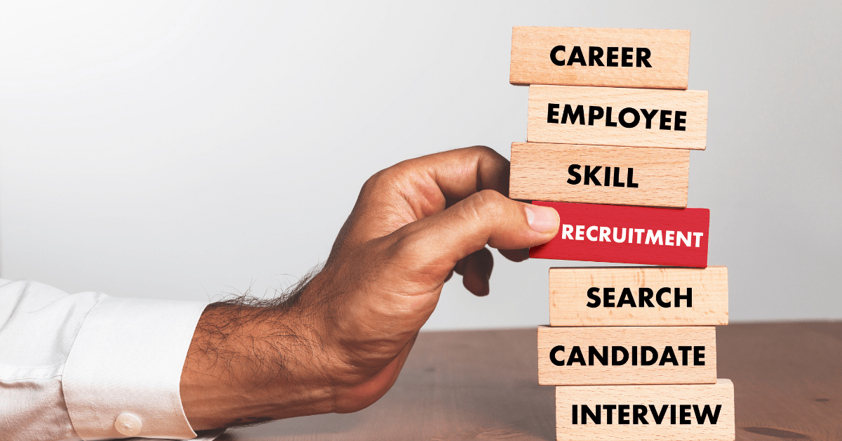 Stack of blocks with one red one that says "Recruitment." Hand grabbing it from the stack.