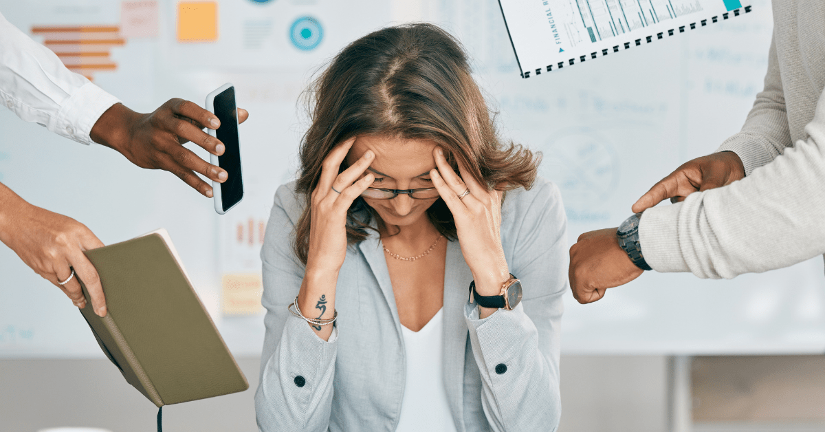 Employee looks stressed, holds her head, stares down at her desk